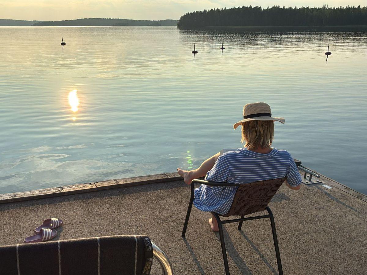 Aurinkoinen järvimasema, ihminen hattu päässä istumassa tuolissa auringossa.