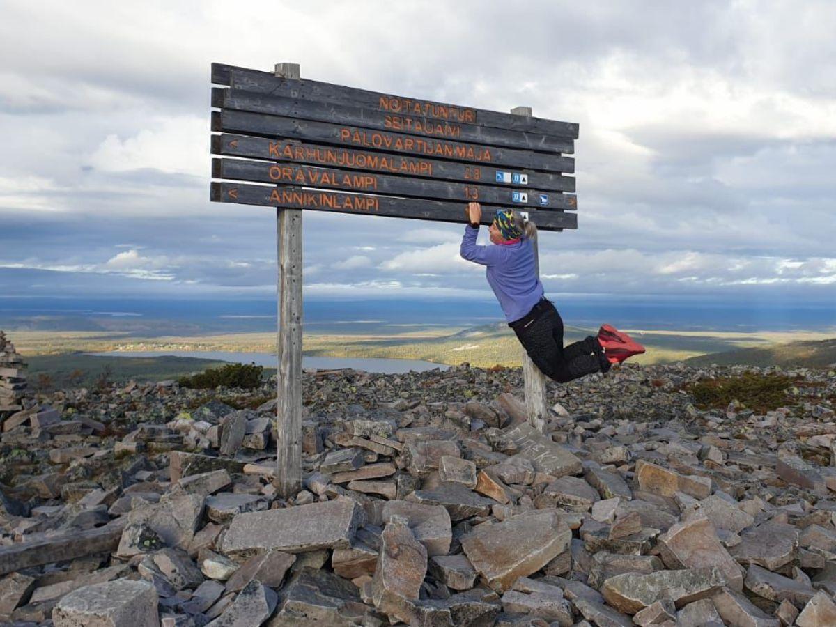 Lapin tunturimaisemassa kyltti, josta henkilö roikkuu hymyillen.